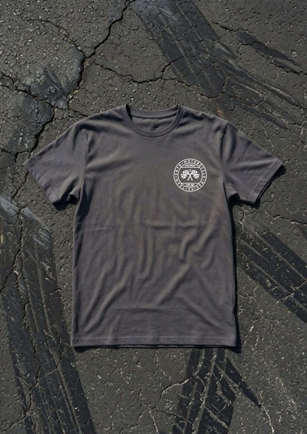 A dark gray crewneck t-shirt with a circular white chest graphic, laid flat on a cracked asphalt surface.