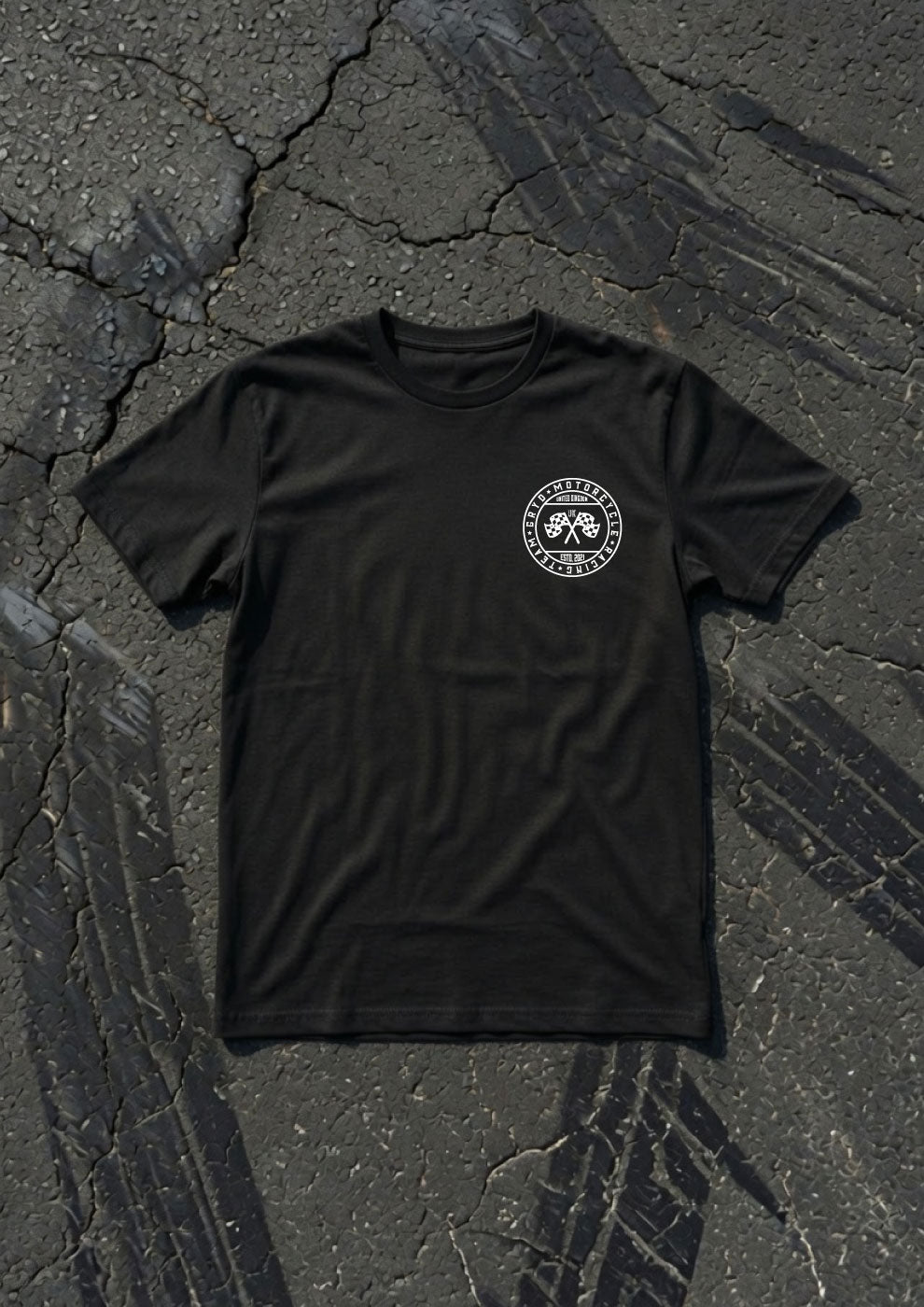 A black short-sleeve t-shirt with a circular white graphic on the left chest, laid flat on a textured dark asphalt surface.