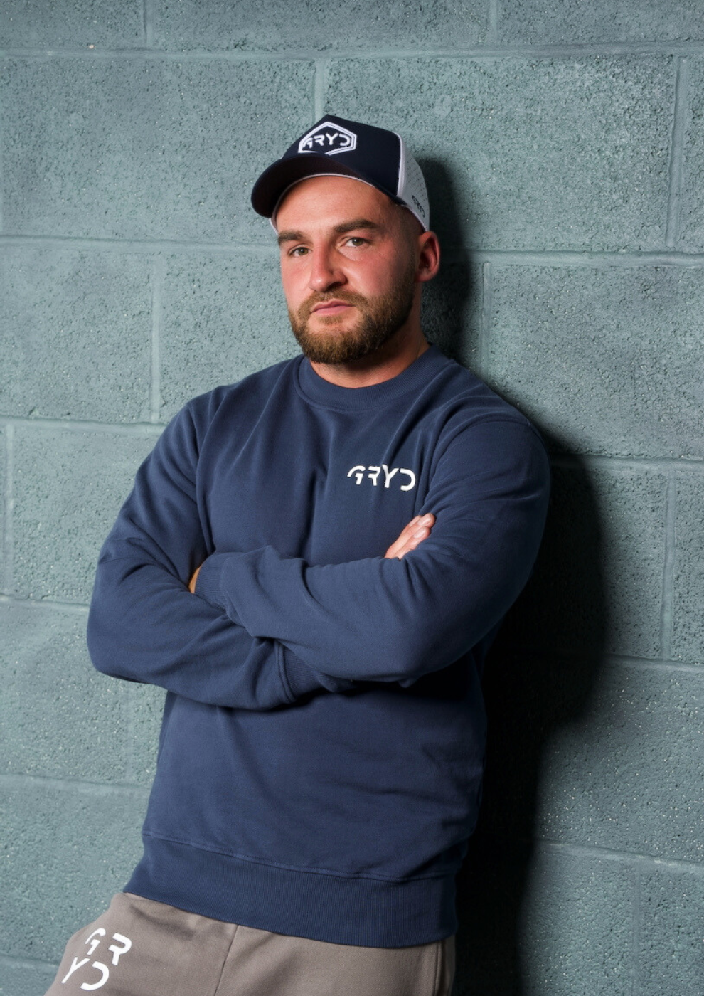 Man wearing a navy blue sweatshirt and cap against a gray brick wall