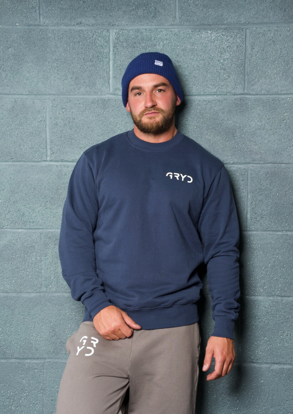 Man wearing a navy blue sweatshirt with 'ARYD' logo against a gray brick wall