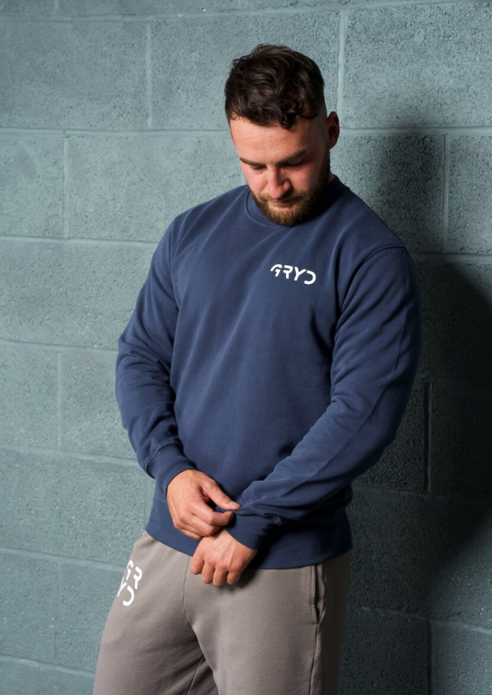 Man wearing a navy blue sweatshirt with a logo against a gray wall